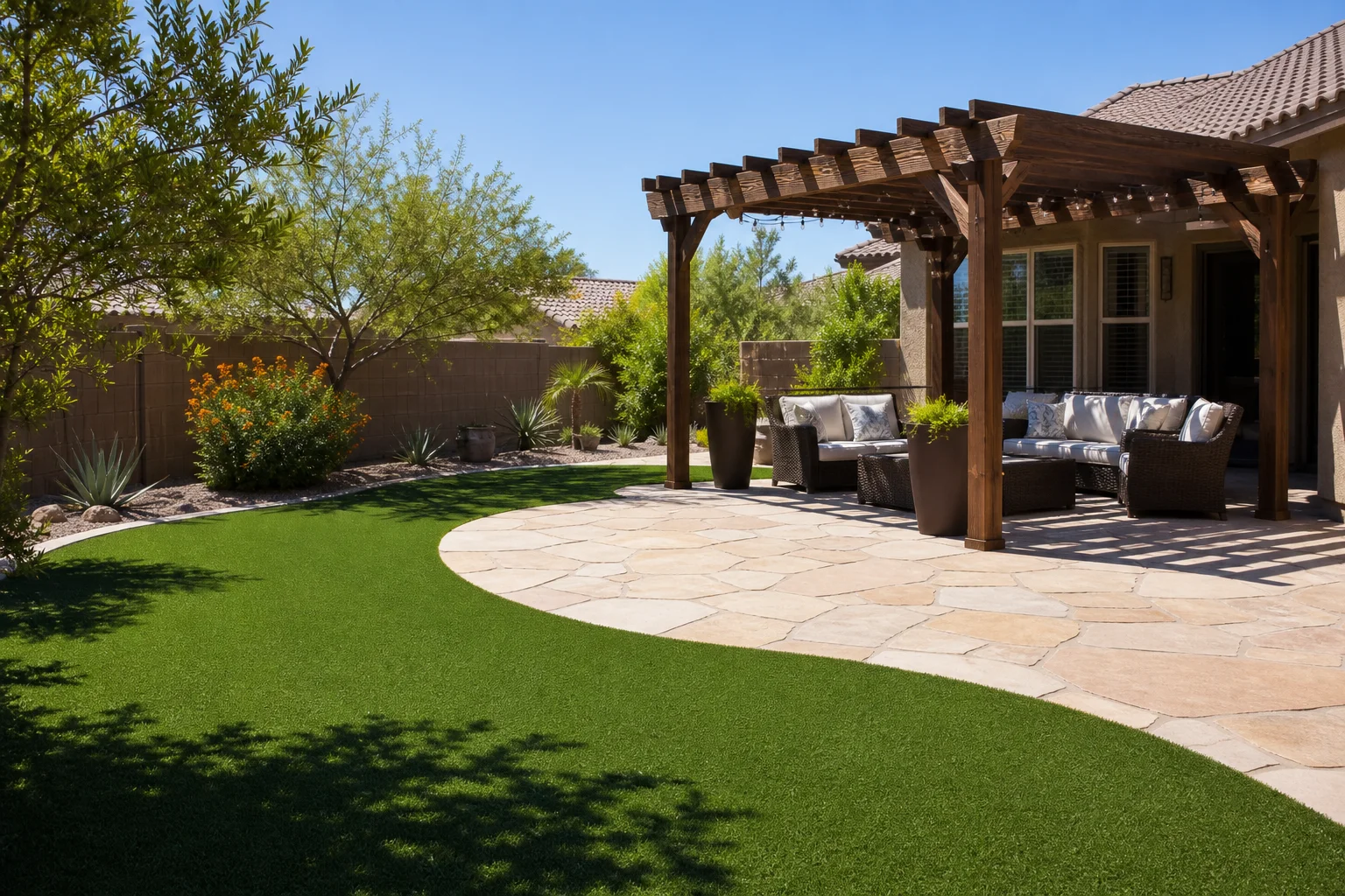 Completed Phoenix-area residential backyard featuring a large artificial grass installation alongside flagstone pavers, a pergola, and desert landscaping surrounding the home exterior